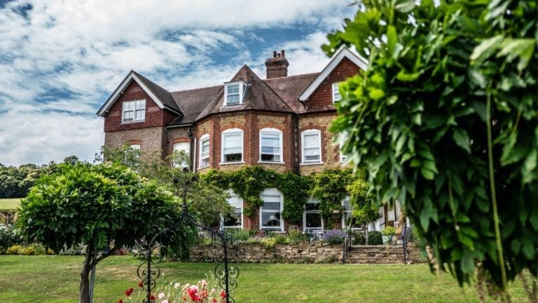 Close up of the front aspect of Birtley House Nursing Home showing the Bay windows of the Birtley House West Wing rooms from the garden and fresh flowers along the terrace