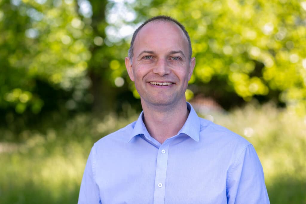 Headshot of Tim Whalley a Nominated Individual at Birtley House Nursing Home smiling in a shirt in front of a blurred outdoor background